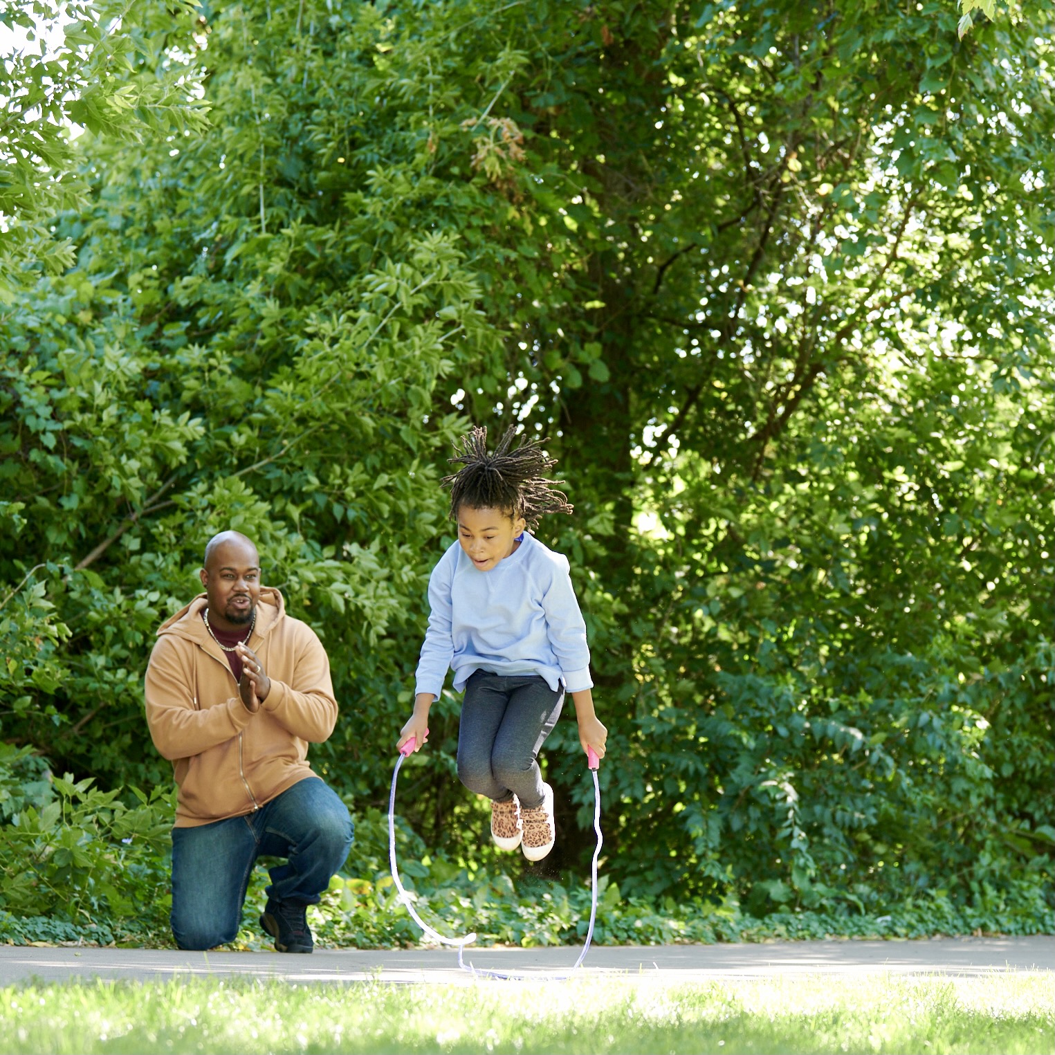 Father teaching daughter to jump rope outside on a summer day